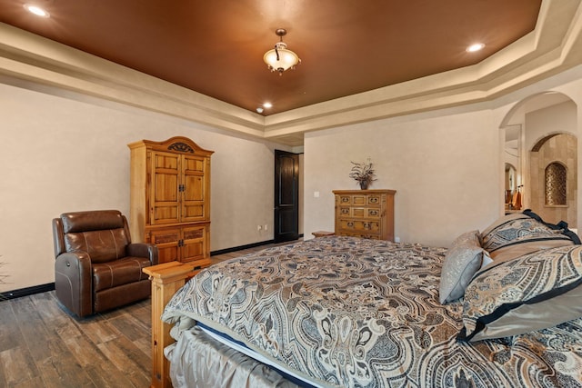 bedroom with arched walkways, baseboards, a tray ceiling, and wood finished floors