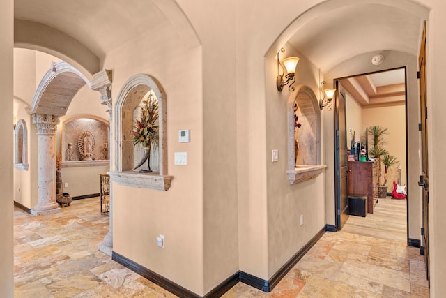 hall featuring stone tile flooring, arched walkways, and baseboards