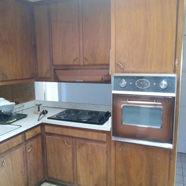 kitchen with stainless steel oven, black electric stovetop, under cabinet range hood, and light countertops