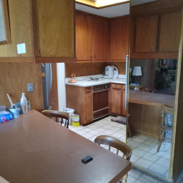 kitchen featuring light tile patterned floors, oven, brown cabinets, and light countertops