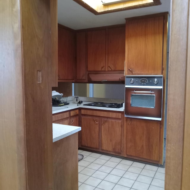 kitchen featuring oven, under cabinet range hood, brown cabinetry, light countertops, and black electric cooktop