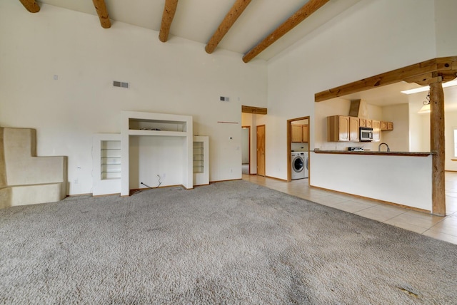 unfurnished living room with beamed ceiling, light carpet, light tile patterned floors, washer / dryer, and a towering ceiling