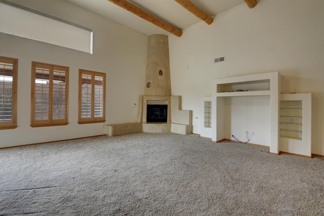 unfurnished living room featuring visible vents, carpet floors, a high ceiling, and beam ceiling