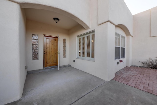 view of exterior entry featuring stucco siding and a patio area