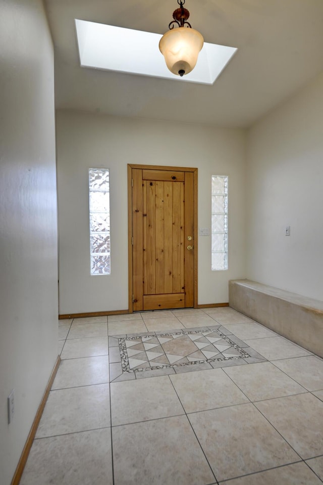 entryway with a skylight, light tile patterned flooring, a healthy amount of sunlight, and baseboards