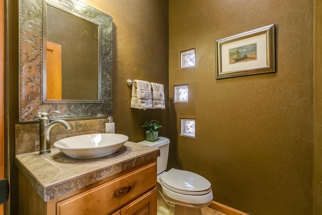 half bathroom with vanity, toilet, and a textured wall