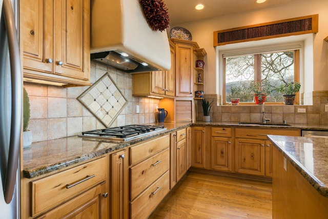 kitchen featuring premium range hood, a sink, stainless steel appliances, light wood-style floors, and stone counters