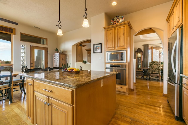 kitchen with light wood-style flooring, a kitchen island, arched walkways, and stainless steel appliances