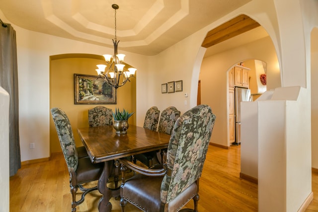 dining area featuring arched walkways, light wood-style flooring, a raised ceiling, and baseboards