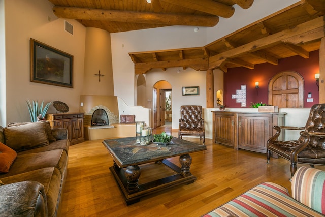 living room featuring a fireplace with raised hearth, beam ceiling, wood ceiling, and wood finished floors