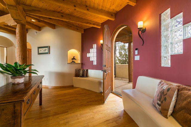 hallway featuring light wood-type flooring, beam ceiling, arched walkways, baseboards, and wood ceiling