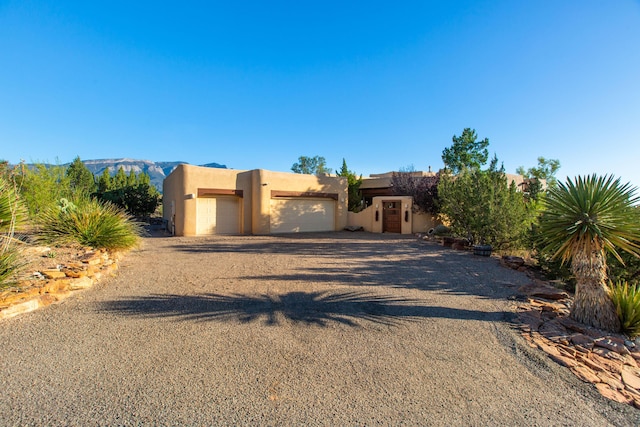 pueblo revival-style home featuring stucco siding, driveway, and an attached garage