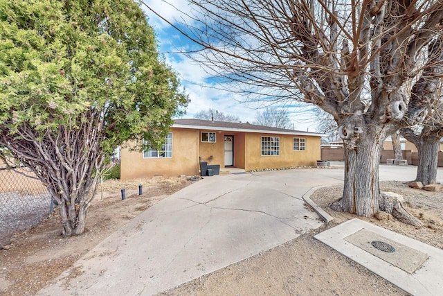 view of front facade featuring stucco siding, driveway, and fence