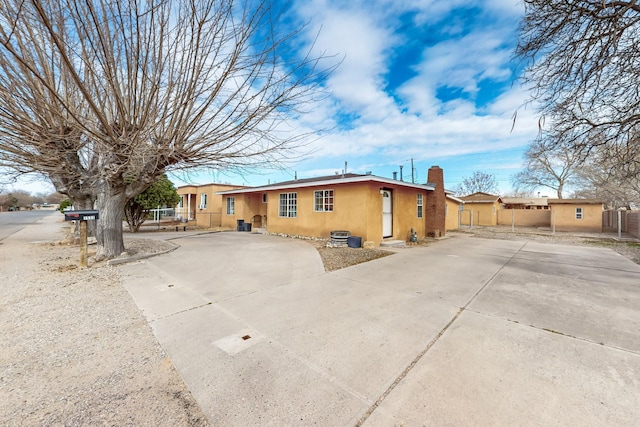 view of front of home featuring concrete driveway, fence, a chimney, and stucco siding