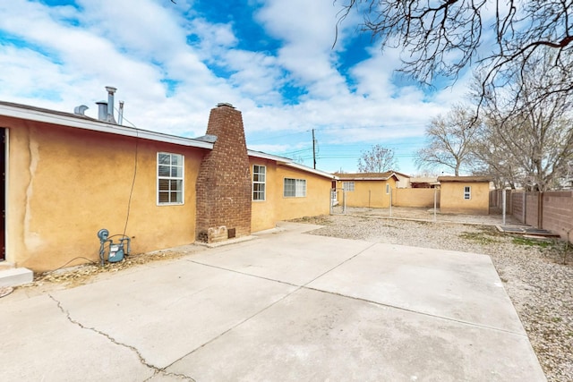 rear view of property with stucco siding, a patio area, a chimney, and fence