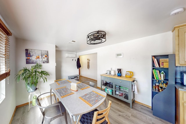 dining space with visible vents, baseboards, light wood-style floors, and a wall unit AC