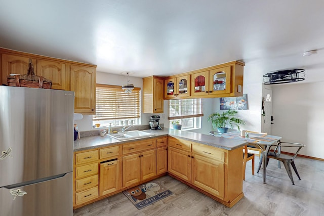 kitchen with a sink, freestanding refrigerator, a peninsula, light wood finished floors, and light countertops