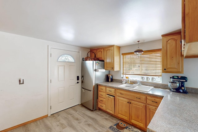 kitchen with light countertops, light wood-style flooring, freestanding refrigerator, and a sink