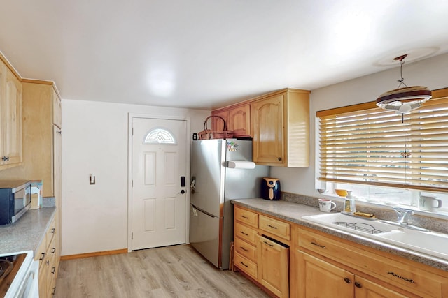 kitchen with light brown cabinetry, light countertops, light wood-type flooring, appliances with stainless steel finishes, and a sink