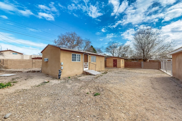 rear view of property featuring stucco siding, an outbuilding, and fence