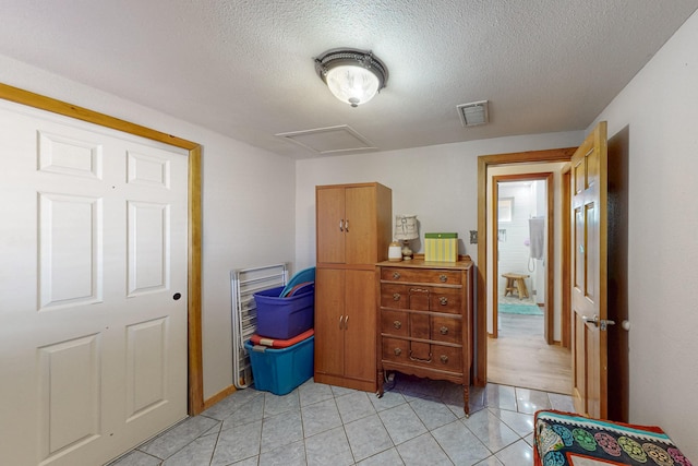 interior space featuring visible vents, a textured ceiling, attic access, and light tile patterned flooring