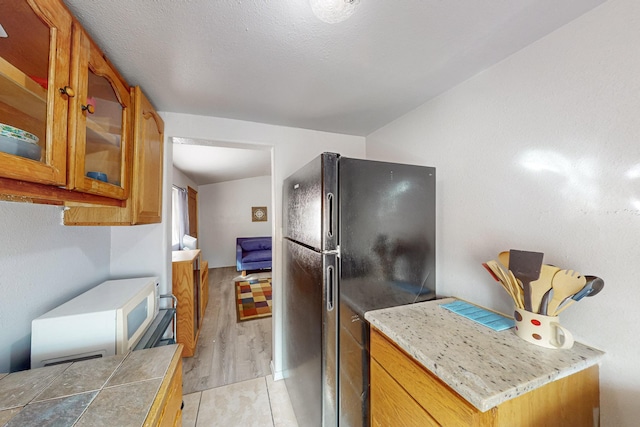 kitchen featuring glass insert cabinets, light countertops, brown cabinets, freestanding refrigerator, and light wood-style floors