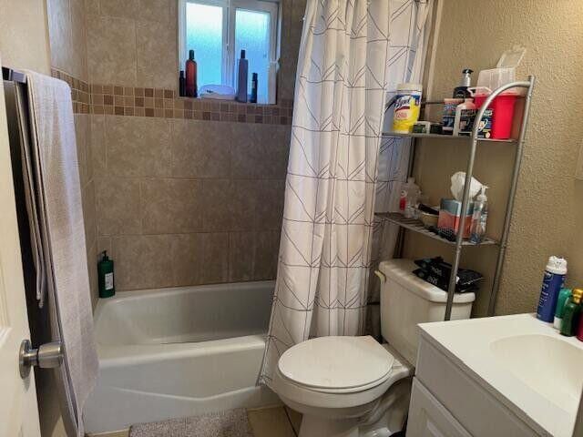 full bath with vanity, toilet, a textured wall, and shower / tub combo with curtain