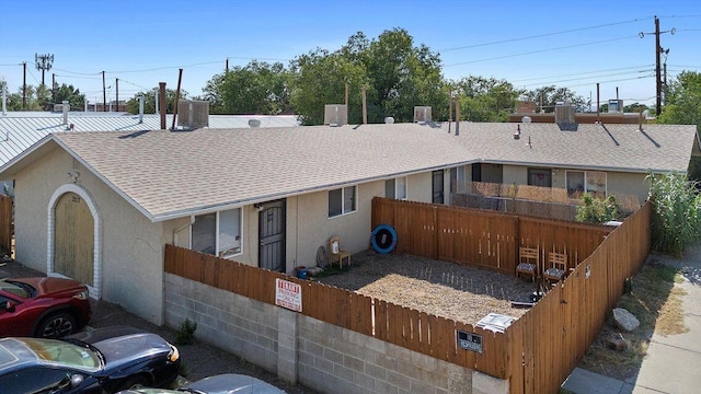 ranch-style house featuring stucco siding, a shingled roof, and fence