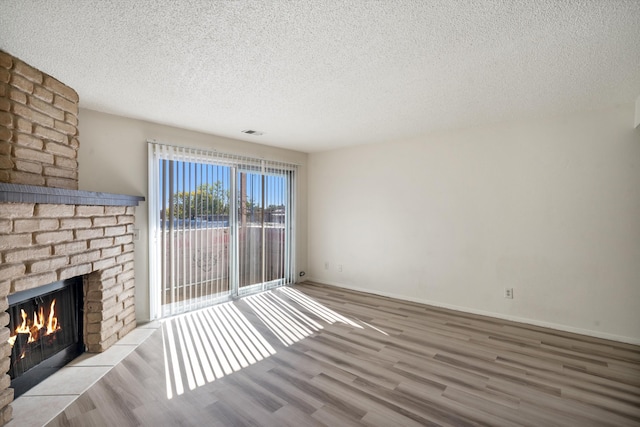 unfurnished living room featuring wood finished floors, visible vents, baseboards, a fireplace, and a textured ceiling