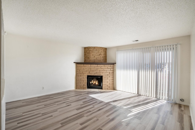 unfurnished living room featuring visible vents, a fireplace, a textured ceiling, and wood finished floors