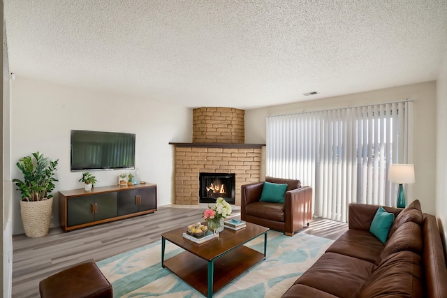 living room with visible vents, a brick fireplace, a textured ceiling, and wood finished floors