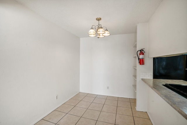 unfurnished dining area with light tile patterned floors, a notable chandelier, and a textured ceiling