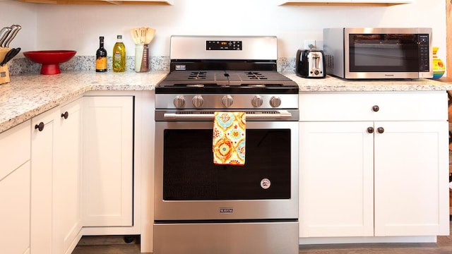 kitchen with light stone countertops, appliances with stainless steel finishes, and white cabinetry