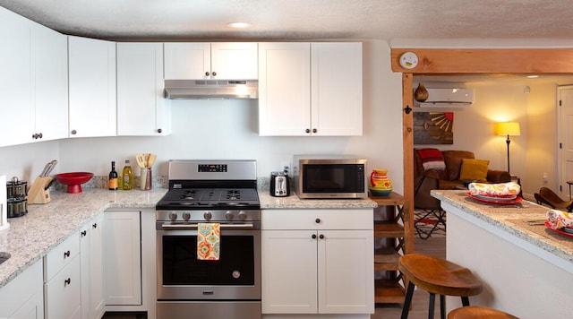 kitchen with recessed lighting, under cabinet range hood, a wall mounted air conditioner, white cabinetry, and appliances with stainless steel finishes