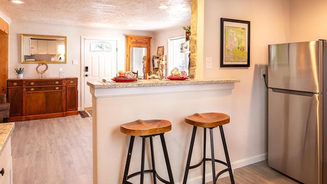 kitchen with a breakfast bar, light wood finished floors, freestanding refrigerator, and a textured ceiling