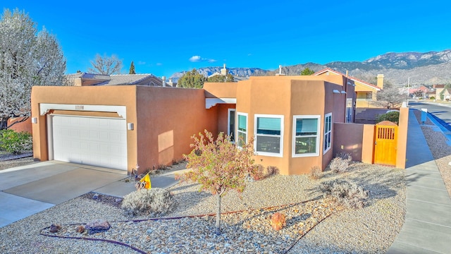 pueblo-style home with an attached garage, stucco siding, driveway, a mountain view, and a gate