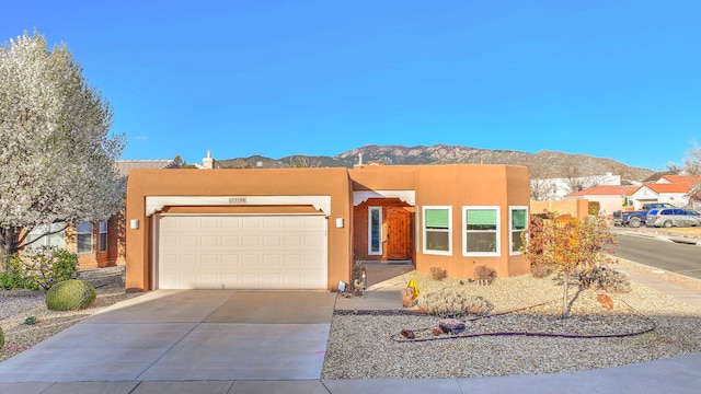 pueblo revival-style home featuring stucco siding, a mountain view, driveway, and a garage