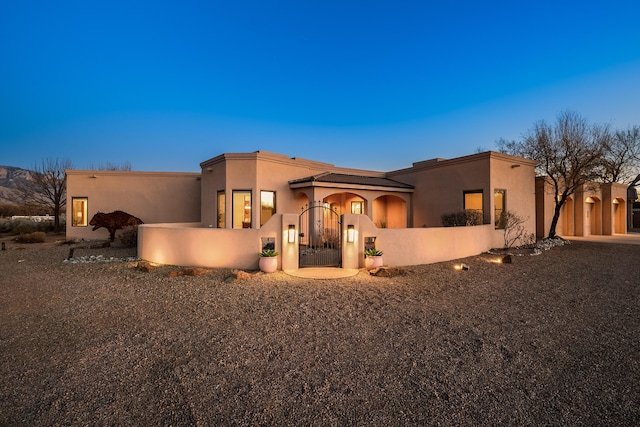 pueblo-style house with a gate, a fenced front yard, and stucco siding