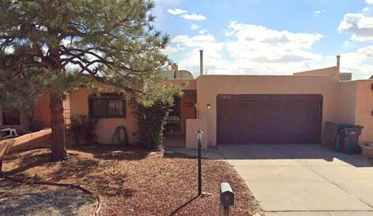 pueblo revival-style home featuring stucco siding, a garage, and concrete driveway