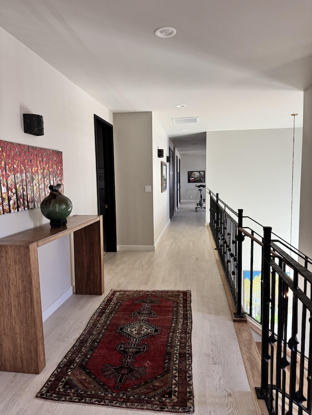 hallway with an upstairs landing, wood finished floors, visible vents, and baseboards