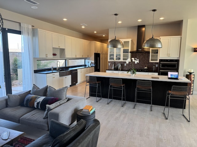 kitchen with light wood finished floors, open floor plan, a breakfast bar, black appliances, and wall chimney exhaust hood