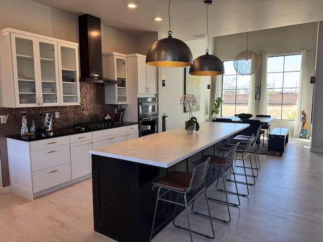 kitchen featuring a kitchen bar, black appliances, a kitchen island, backsplash, and wall chimney range hood