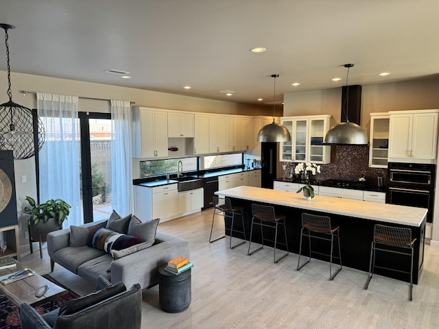 kitchen featuring black appliances, wall chimney range hood, a kitchen breakfast bar, and light wood-type flooring