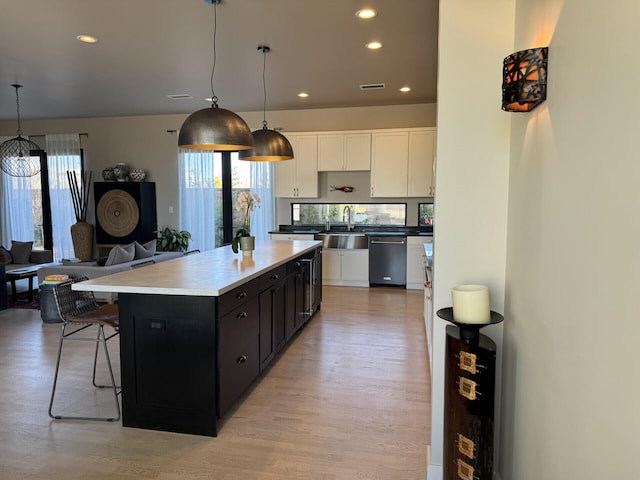 kitchen with white cabinetry, a kitchen island, a sink, light wood-style floors, and dishwasher