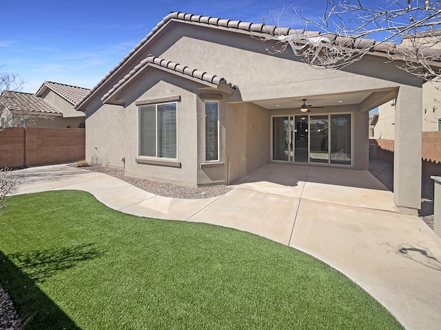 rear view of property with stucco siding, fence, a yard, ceiling fan, and a patio area