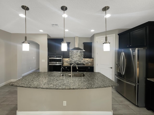 kitchen featuring visible vents, a sink, stainless steel appliances, wall chimney range hood, and tasteful backsplash