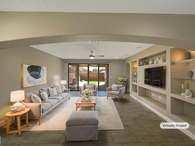 living room featuring built in shelves, a ceiling fan, a textured ceiling, arched walkways, and baseboards