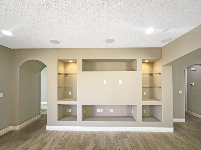 spare room featuring arched walkways, built in features, a textured ceiling, and wood finished floors