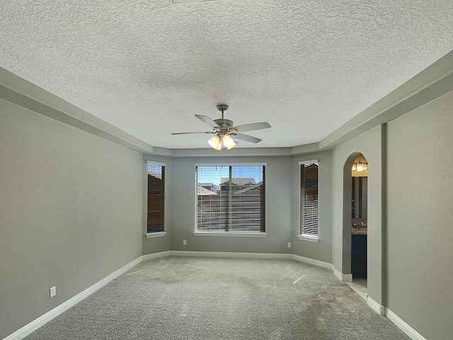 empty room featuring light carpet, a textured ceiling, arched walkways, baseboards, and ceiling fan