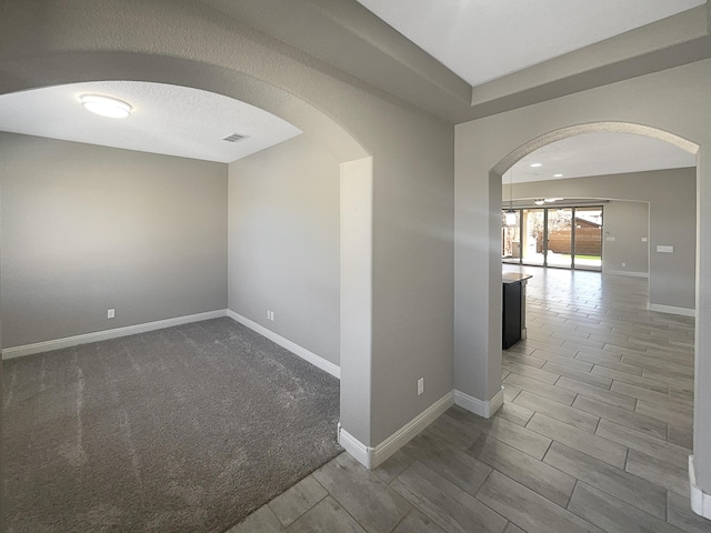 spare room featuring arched walkways, visible vents, a textured ceiling, and baseboards